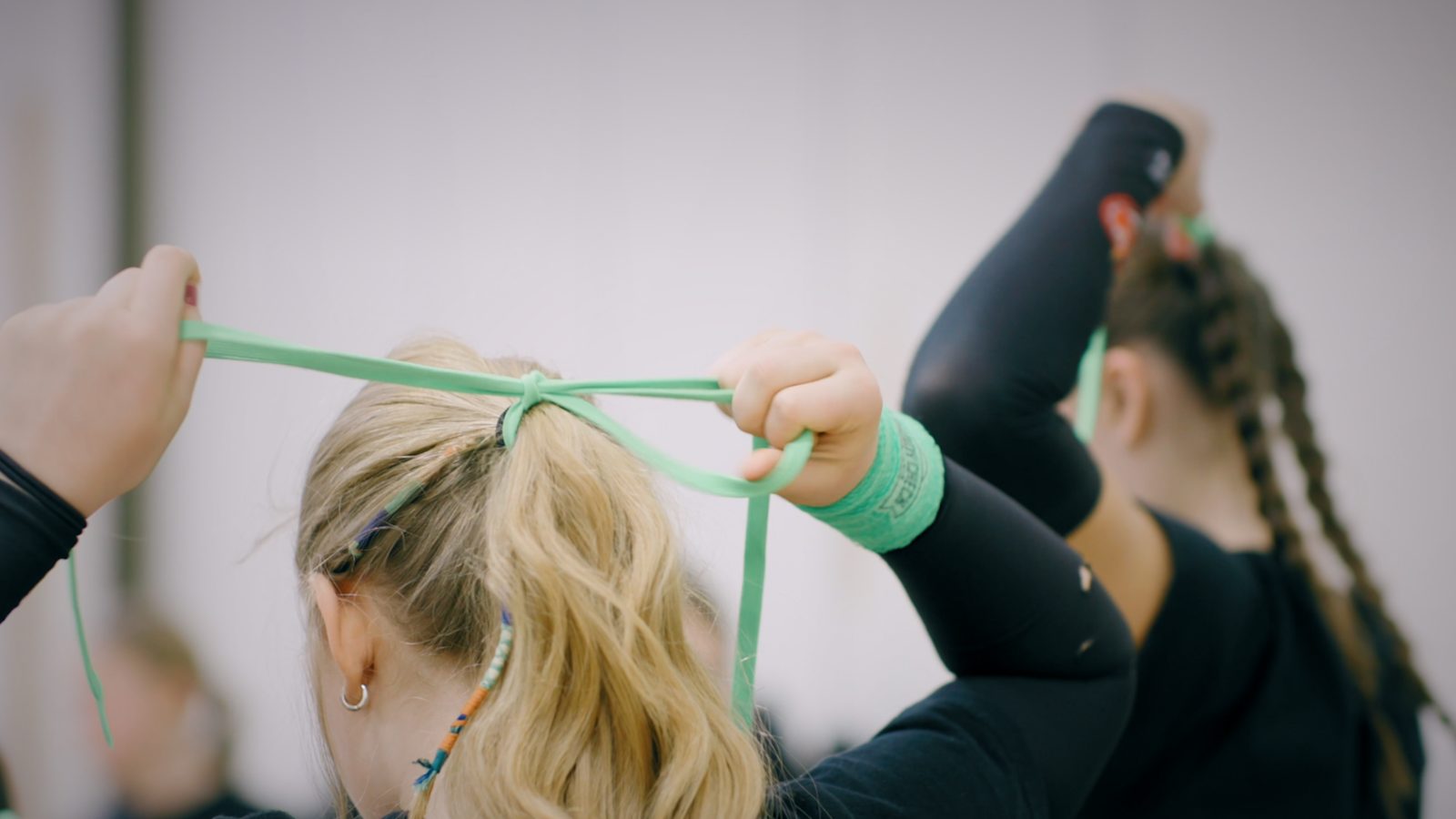 Two athletes tying green ribbons in each other's hair